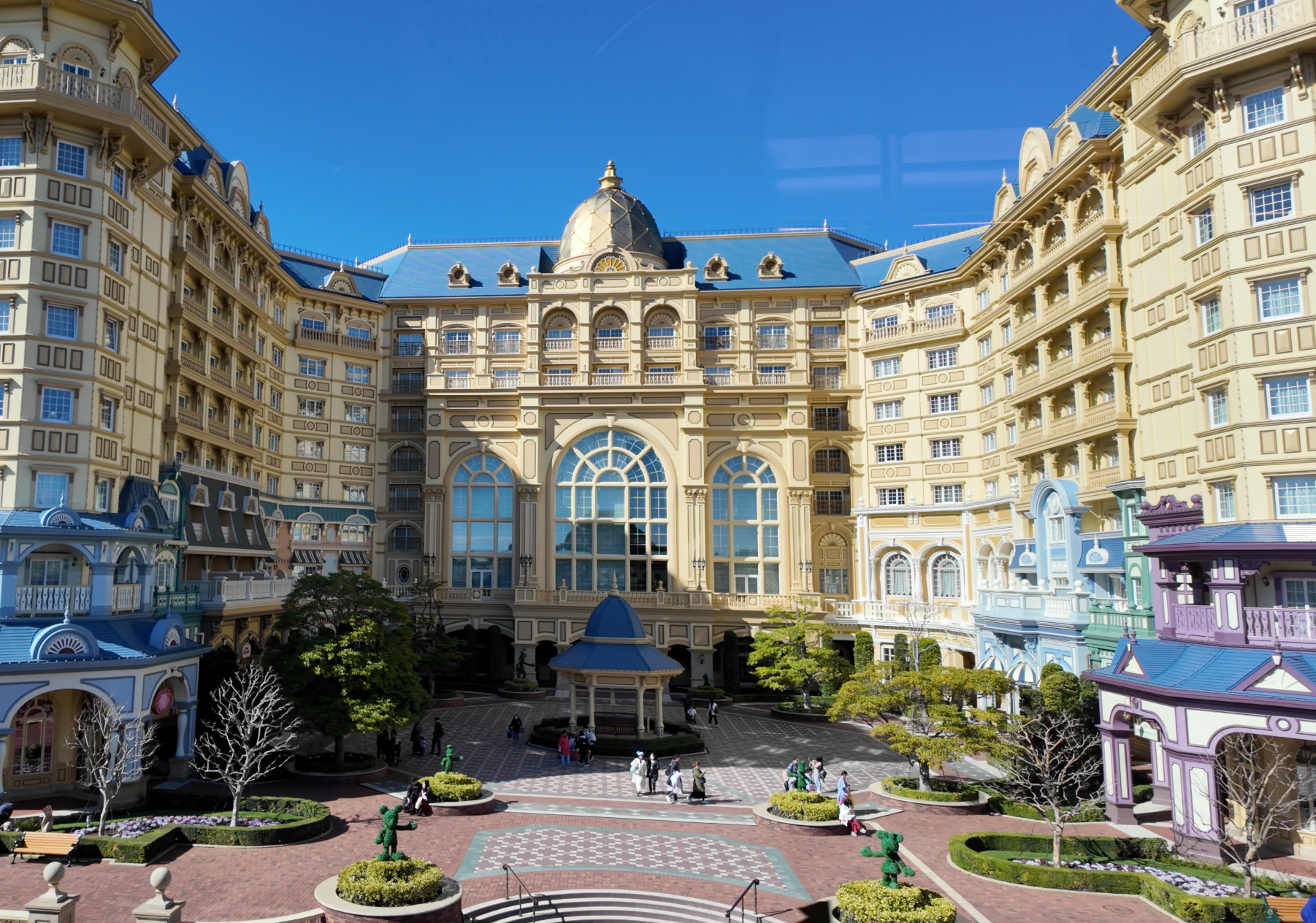 อาคาร Tokyo Disneyland Hotel ล้อมลานด้านหน้า มีหลังคาสีฟ้าและระเบียงสีพาสเทล