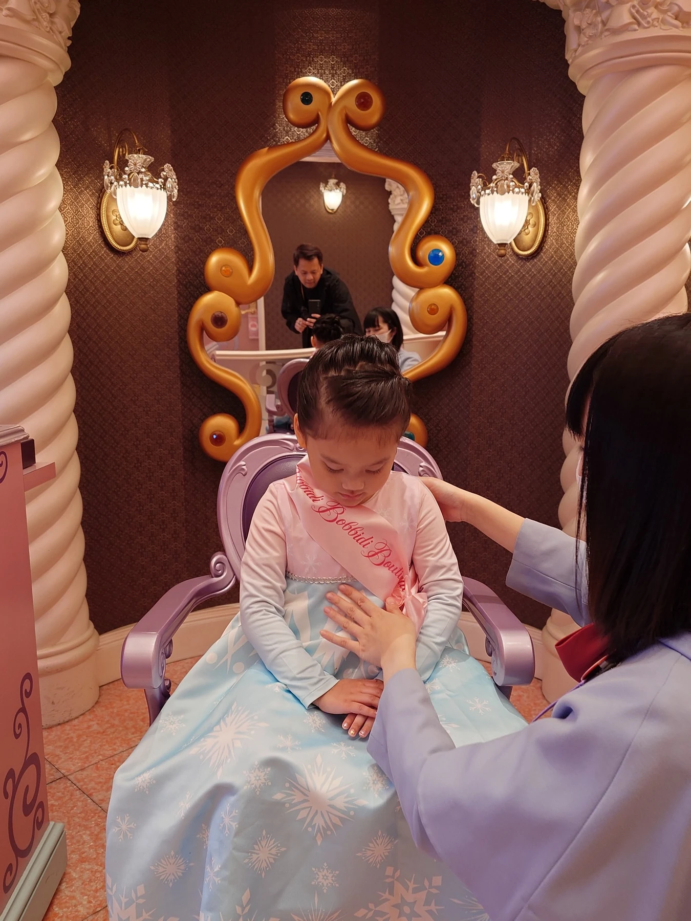 ลูกสาวในชุดเจ้าหญิงนั่งหน้ากระจกหลังทำผม