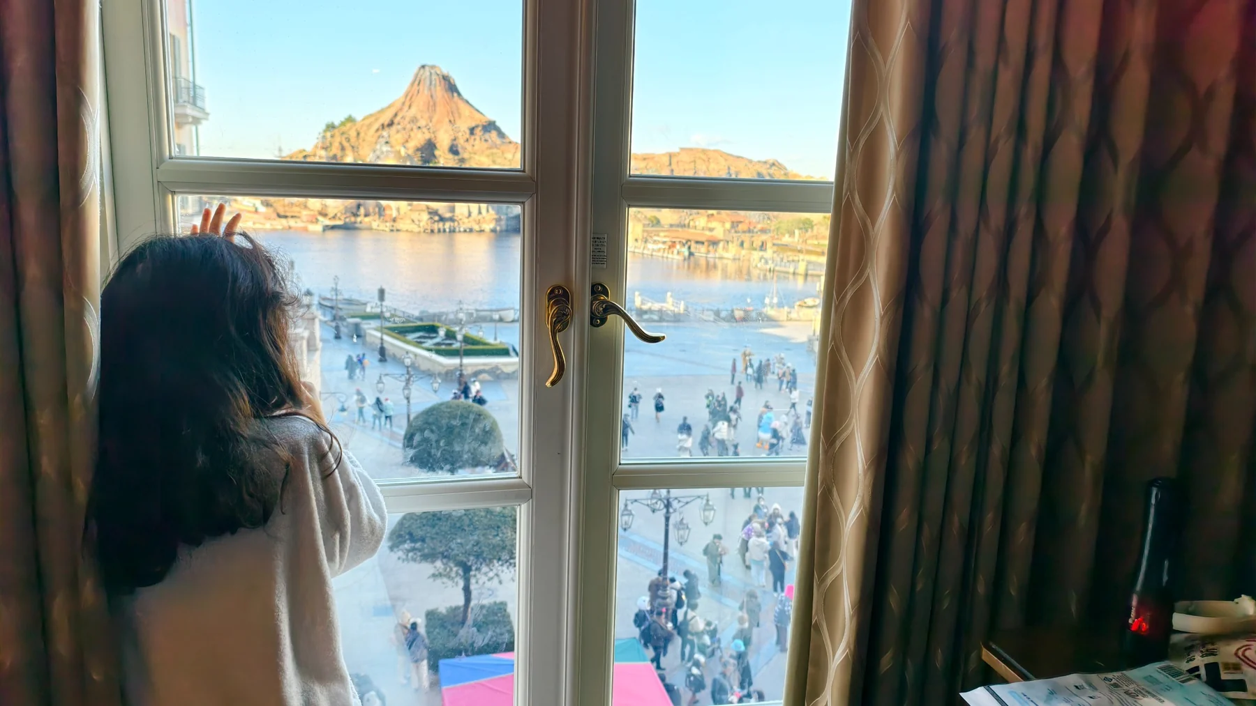 ลูกสาวยืนมองอ่าวและแขกในสวนสนุกจากหน้าต่างห้อง MiraCosta Hotel
