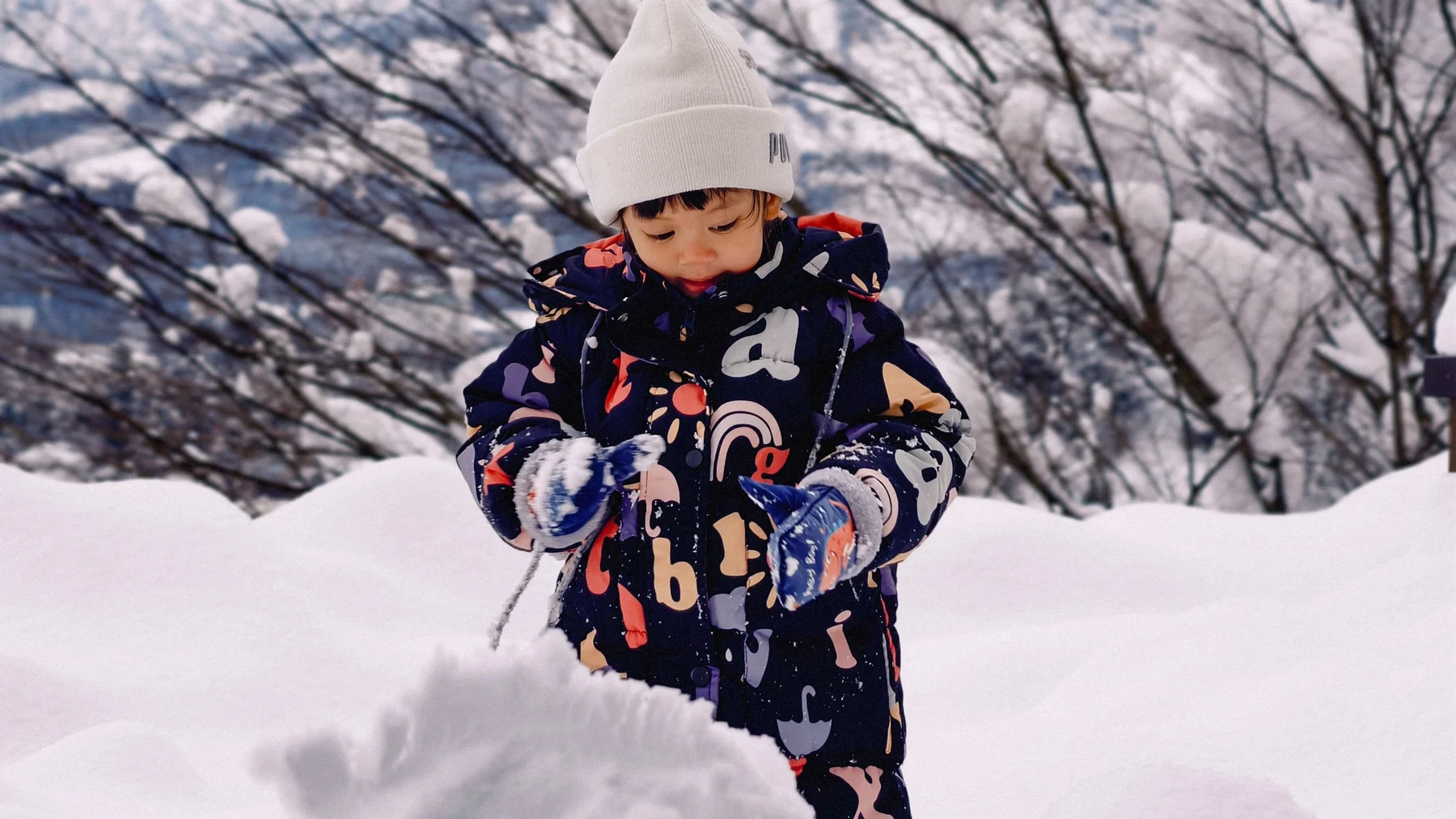 ลูกคนเล็กสวมหมวกสีขาวและชุดกันหนาวยืนจับหิมะ